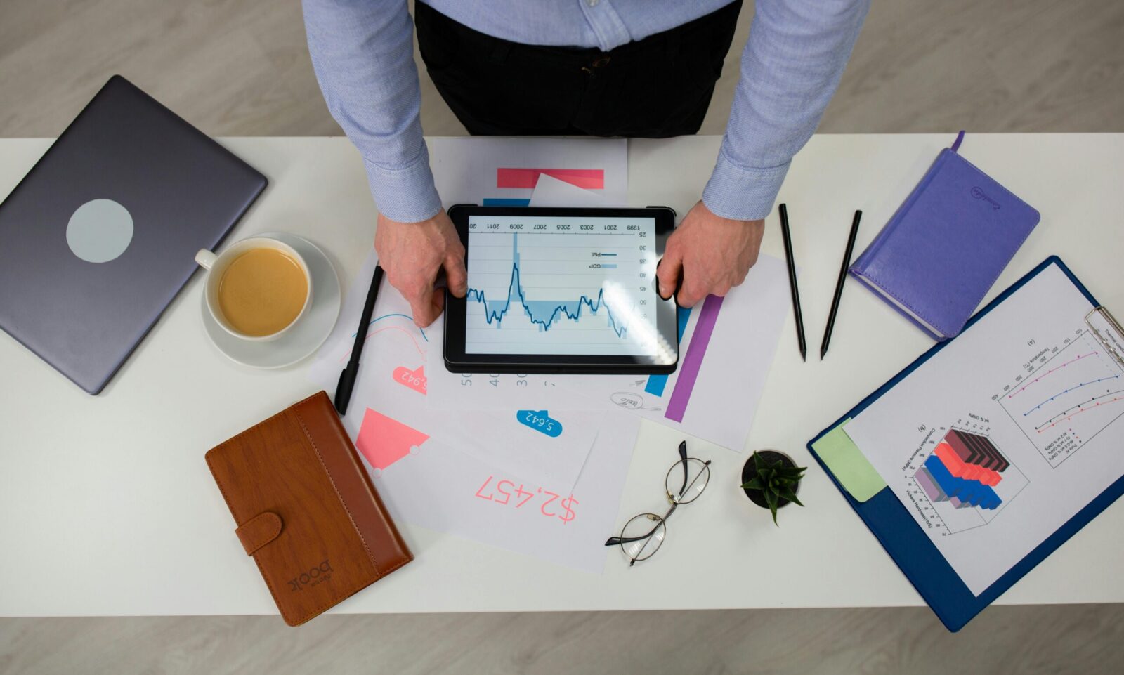 Overhead view of businessman using tablet to review data charts at a modern office desk.